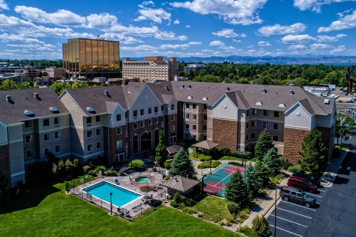 A vibrant outdoor pool area featuring a sparkling swimming pool, adjacent hot tub, and surrounding landscaped gardens. People are seen swimming, sunbathing, and relaxing, with the hotel facade in the background and opportunities for social interaction and recreation.