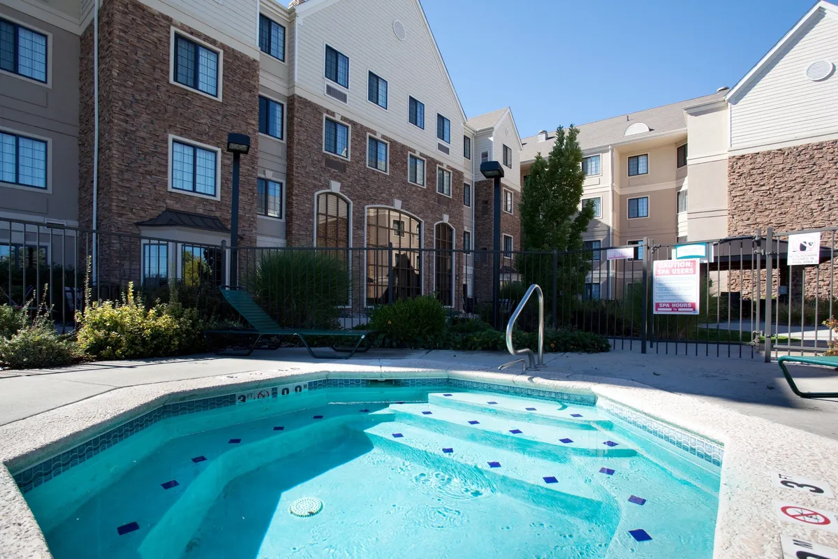A beautifully landscaped pool and hot tub area, with guests relaxing at sunset. The building's facade forms the backdrop, while the outdoor amenities and garden highlight spaces for leisure and relaxation right at the property.
