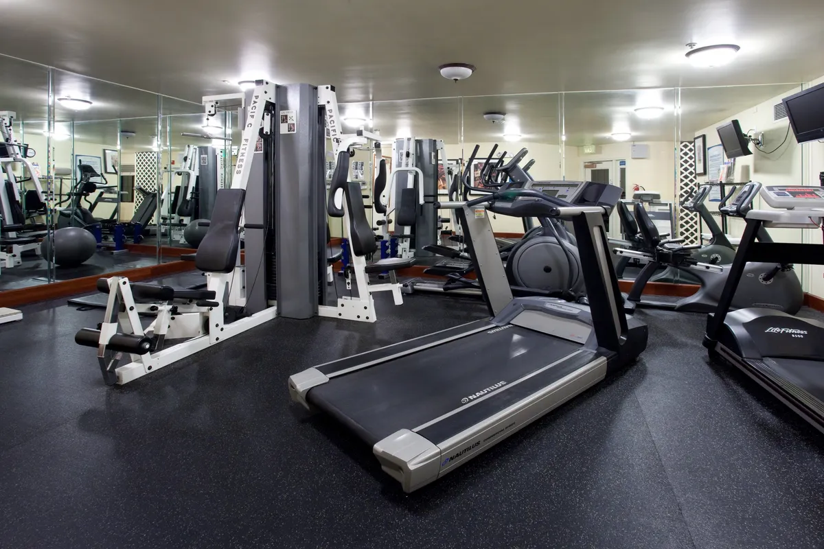 A modern, well-equipped fitness center featuring treadmills, weight machines, exercise balls, and mirrored walls. The environment is bright and motivating, with ample space for both individual workouts and group fitness activities.
