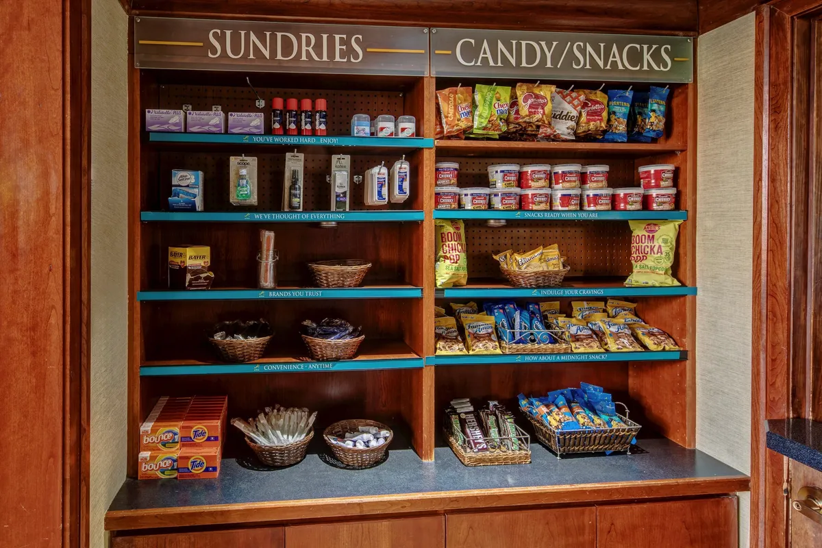 This image features shelves stocked with sundries and snacks, showcasing a variety of colorful packaged products and baskets filled with assorted items. The environment looks convenient and welcoming, inviting guests to browse and pick up essentials or treats.