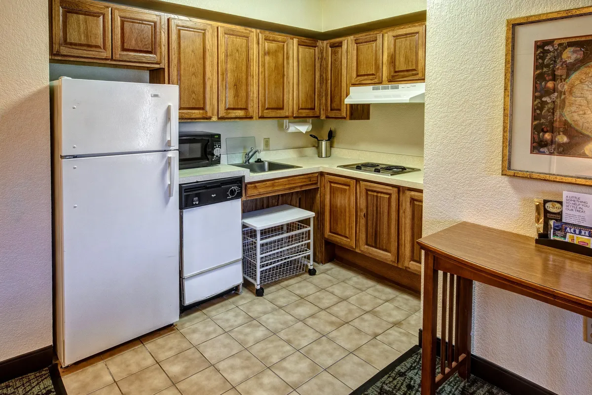 This image showcases a functional and cozy kitchen and dining area, featuring a modern refrigerator, ample cabinet space, a sink, and a stove. The table is positioned to allow for both casual meals and social gatherings, capturing the essence of home-cooked meals and togetherness. Natural light brings warmth to the space, making it ideal for morning coffee or evening dinners.