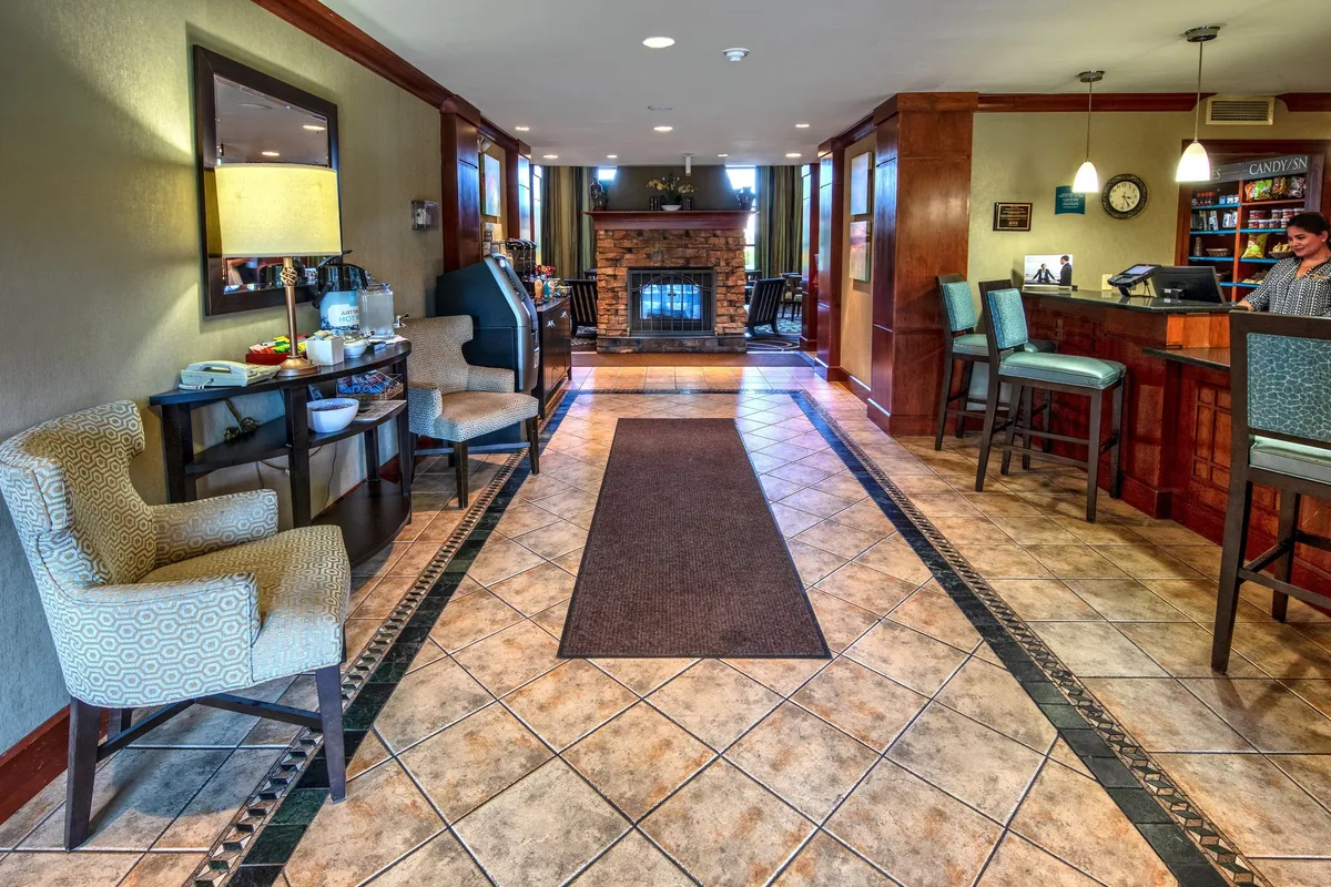 An elegantly designed interior common area with a cozy fireplace, tastefully arranged seating, a reception desk, and a decorative lamp. The space exudes comfort, warmth, and hospitality, suggesting a relaxing atmosphere after a day of urban exploration.