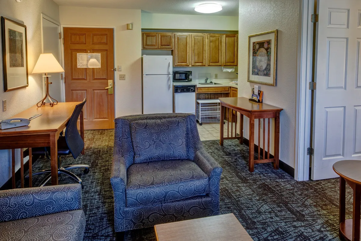 The image showcases a bright, inviting living space with a plush sofa, a modern kitchen area, a convenient desk setup for work or planning adventures, and stylish artwork on the wall. The open layout allows for relaxation, cooking, socializing, or catching up on work—all in the comfort of a thoughtfully designed condo.