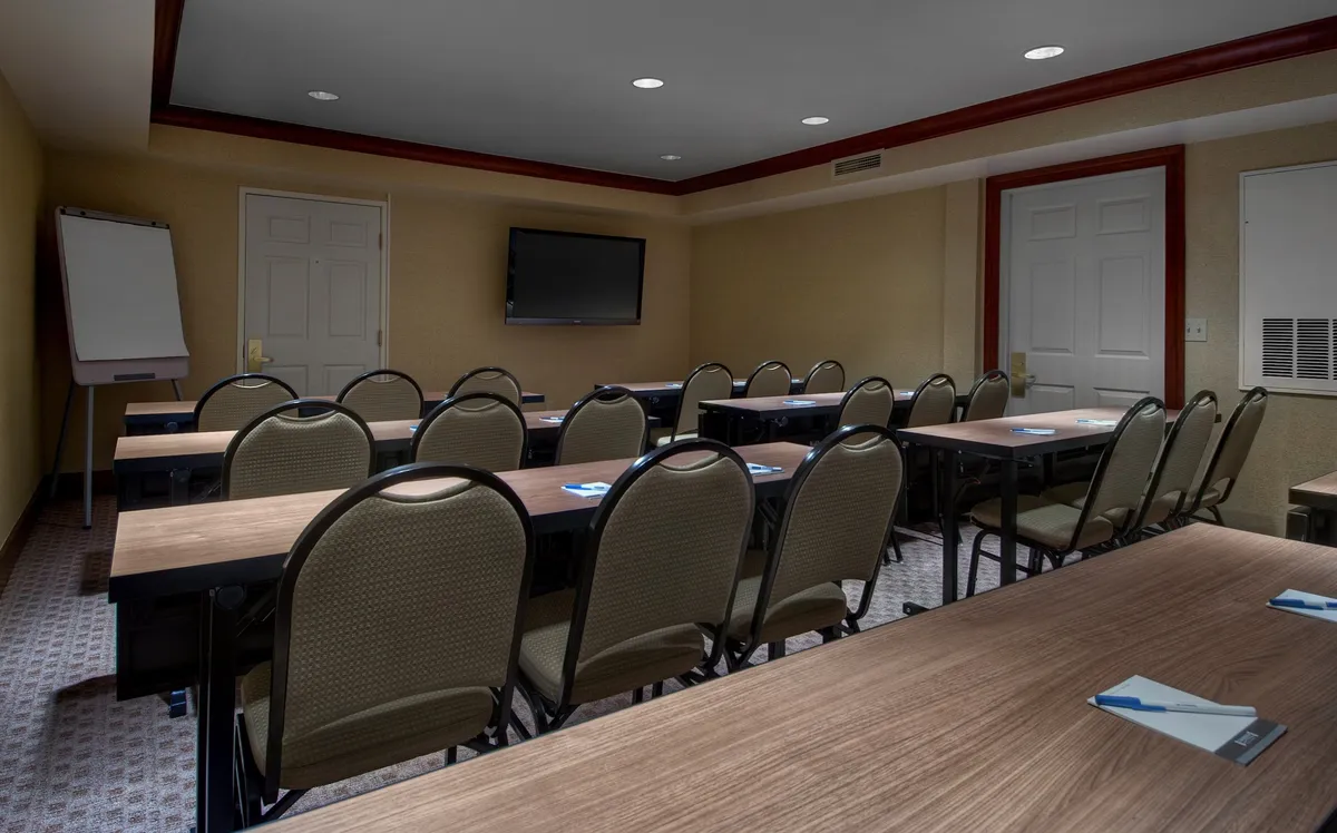 A contemporary meeting room with rows of tables and rounded chairs facing a large presentation screen, creating an environment suited for seminars, workshops, and collaborative sessions.